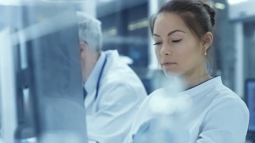 Medical Research Scientist Looks at the Test Tube Results and Types Extracted Data into Her Compute