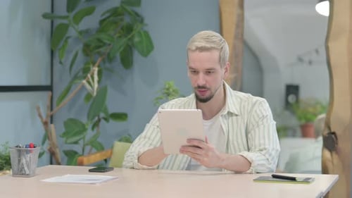 Young Adult Celebrating Success Using Tablet at Desk