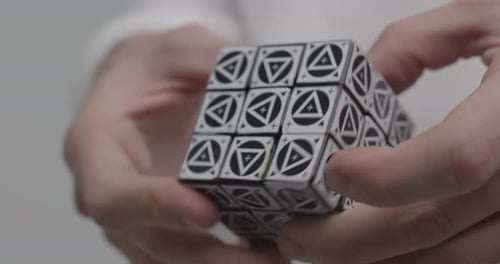 Un hombre resuelve un rompecabezas de cubos de Rubik con varios triángulos en los lados