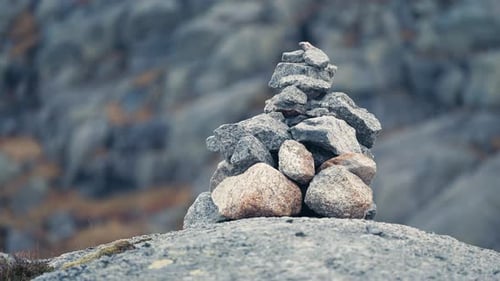 Close-up shot of the stone cairn. Gloomy landscape in the background. Slow-motion, pan left.