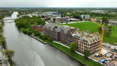 Una toma aérea de una obra en construcción junto a un río en Elbląg, con edificios parcialmente terminados y un