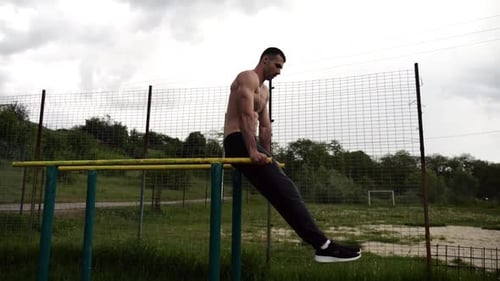 Un homme fort entraîne ses muscles abdominaux en soulevant les jambes sur des barres parallèles sur un terrain de sport pour jeunes torse nu