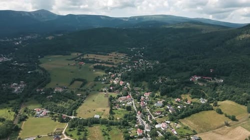 Aerial View of Rural Village and Green Valley Near Mountain Range in Summer