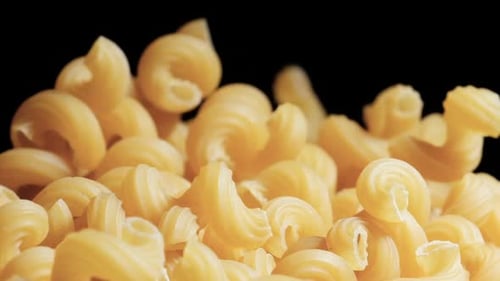 Raw macaroni pasta falls gracefully in stunning slow motion.