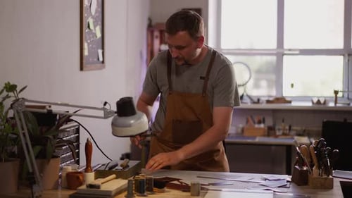 Thoughtful Man in Workwear Seeks Sharpening Tool in Shop