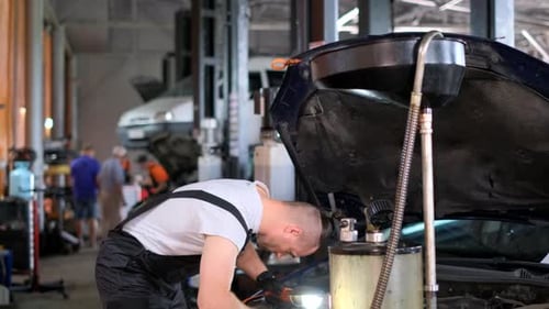 An Individual Examines a Vehicles Engine Inside a Buildings Garage