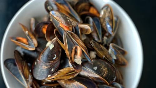Close vertical view of a plate with cooked mussels. Slow motion