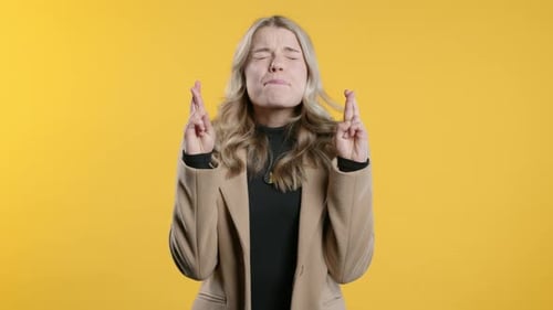 Blond Woman With Fingers Crossed Against Yellow Background