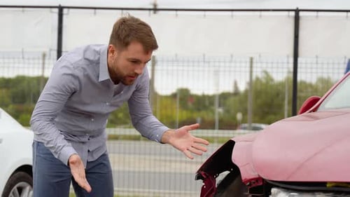 Upset Man Inspects Damaged Red Car After Accident