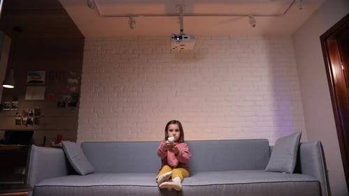 Ein kleines Mädchen zu Hause auf dem Sofa wechselt die Fernsehkanäle mit einer Fernbedienung