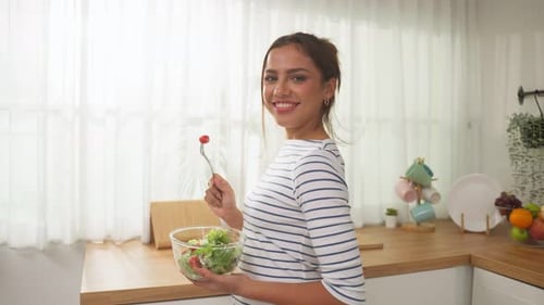Portrait of young Caucasian girl eating green salad in kitchen at home.