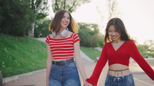 Two Beautiful Young Women Walk Down the Street or Park Holding Hands A Couple of Girls Walk Hand in