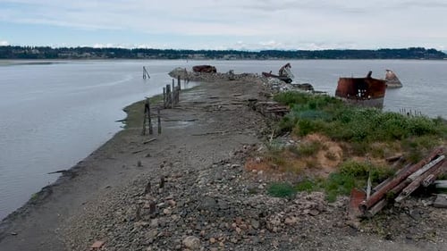 Altes verlassenes Metallboot an der Küste mit altem Dock, Berge im Hintergrund.