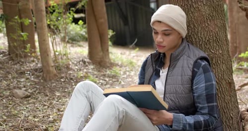 Asiatischer Mann sitzt unter einem Baum und liest ein Buch im Freien und genießt einen friedlichen Moment
