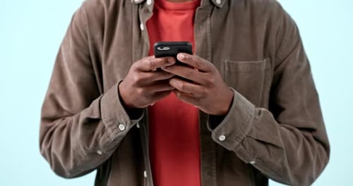 Hands, phone and man typing in studio isolated on blue background