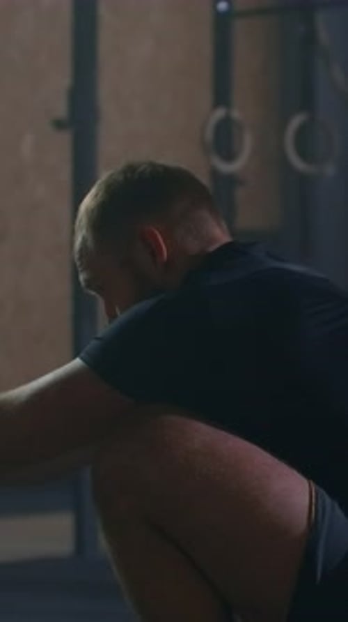 Focused Bearded Athlete Training on Rowing Machine in Dimly Lit Gym Emphasizing Strength Endurance