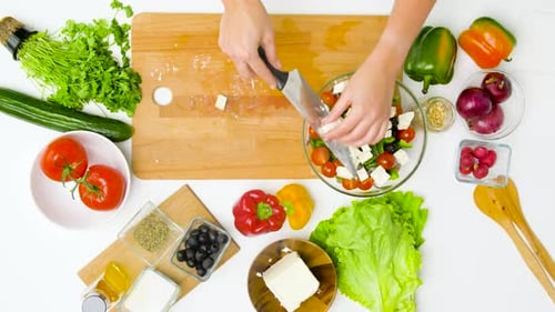 Jeune femme préparant une salade grecque avec du fromage feta dans sa cuisine à la maison