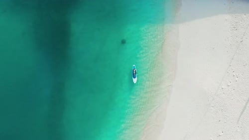 Ein kleines Mädchen liegt auf einem SUP-Board in türkisfarbenem Wasser mit weißem Sandstrand auf der Insel Fulidhoo in