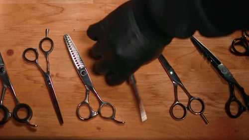 Male Barber Hand in Rubber Glove Choosing Scissors for Haircut From Wooden Table Top View Closeup
