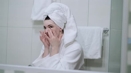A beautiful woman in towel on her head applies Korean mask to moisturize the skin and smoothes it wi