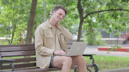 Man Uses Laptop and Stretches Neck on Park Bench