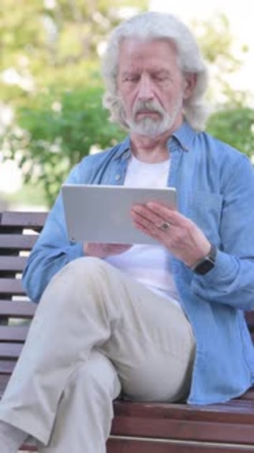 Senior Man Uses Tablet While Sitting on Bench
