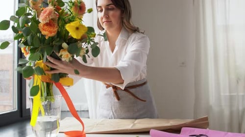 Happy young woman wrapping beautiful spring flowers in craft paper at home