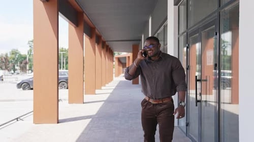 Smiling afro entrepreneur speaking the phone outside the business centre.