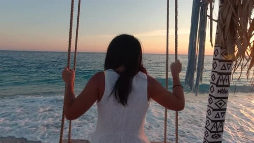 Slow motion girl swinging on bench next to beautiful ocean at sunset