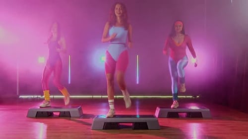 Women Doing Step Aerobics in Studio With Pink Lighting