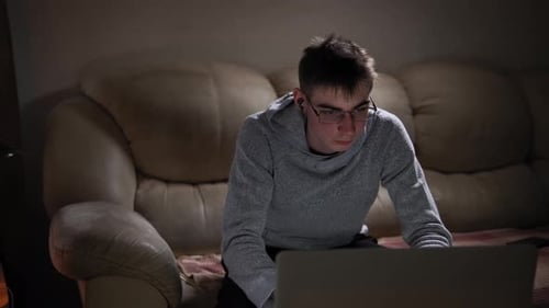 Young Man Works on Laptop at Home in Evening