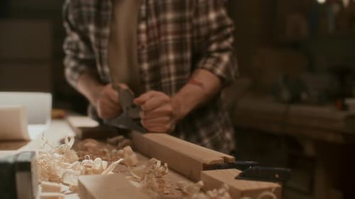 Close Up of Woodworker Smoothing Wood Piece with Hand Plane on Workbench