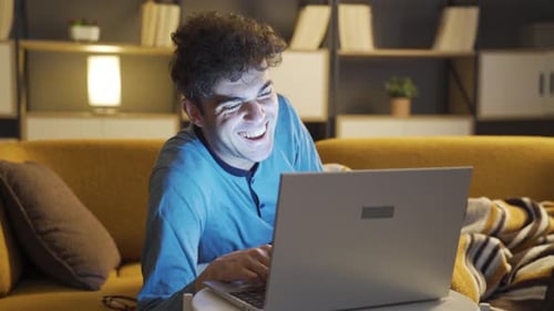 Man Laughing at Laptop on Couch at Night