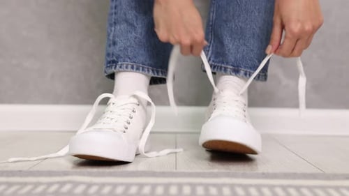 Woman trying on stylish white sneakers indoors, closeup