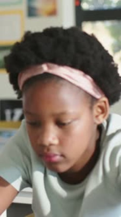 Vertical video: Glancing left, student lowering head and focusing on workbook at classroom desk