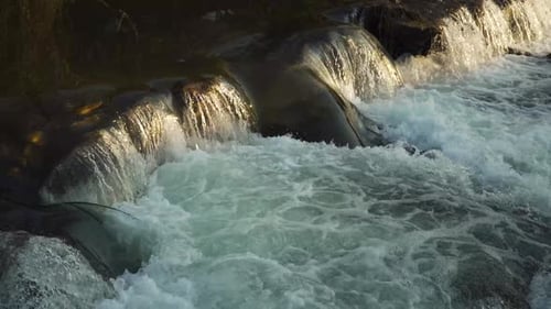 Close up on some water flowing down over a natural dam creating some green and white foam and the se