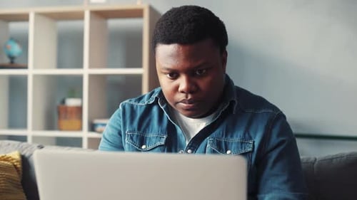 Portrait African American Handsome Man Uses Computer for Work in Home Sit on Sofa Programmer Looks