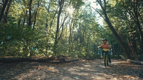 A Boy in a Bicycle Helmet Rides a Bicycle on a Path in the Park
