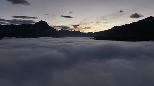 Drone flying above the clouds with silhouettes of the Swiss Alps in the background at a stunning sun