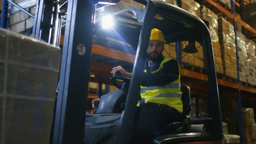 Close-up Shot of a Forklift Driver Operating Vehicle in a Big Warehouse full of Pallet Rack.