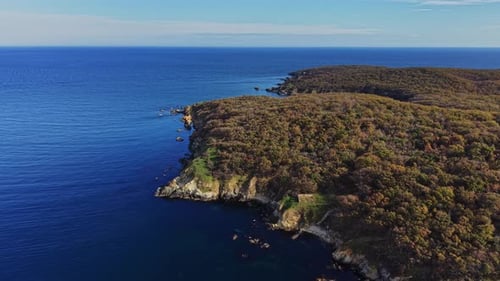 Coastal cliffs meet tranquil blue waters in serene aerial view