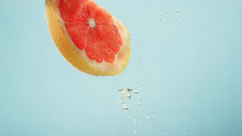 A Piece of Grapefruit Falls Into the Water on a Blue Background
