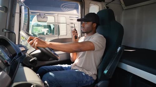 African American Truck Driver Sitting in Cab Speaks on the Radio Walkie Talkie Right Hand Drive Car