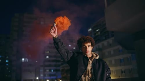 Guy Burning Colored Smoke at Night Sky Signaling Attention in City Closeup