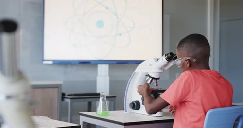 In school, boy using microscope and examining sample in science classroom