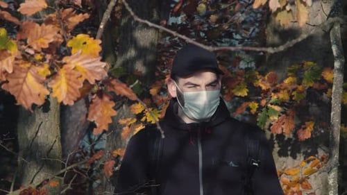 Male tourist wearing face mask in forest walking towards camera, covid pandemic symbolism, middle fr
