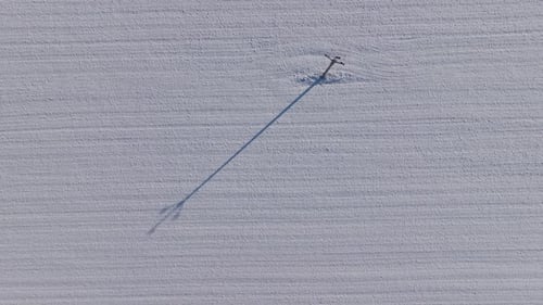 Aerial View of Snowy Field with Electric Pole and Long Shadow