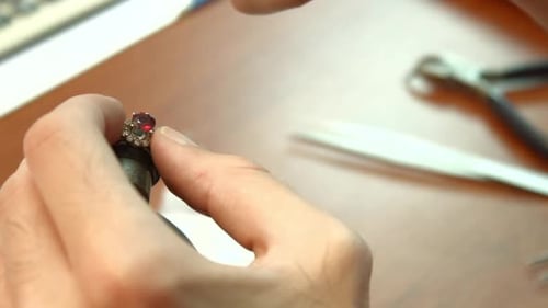 Die Hände des Juweliers stecken einen roten Edelstein in einen schicken goldenen Diamantring