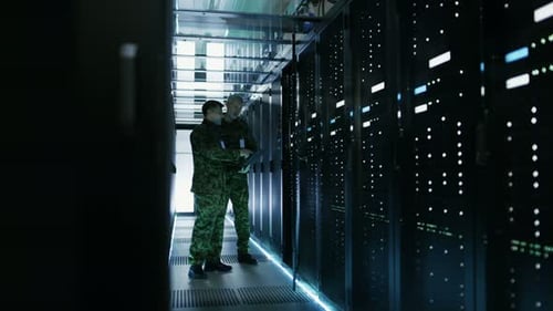 In Data Center Two Military Men Work with Open Server Rack Cabinet. One Holds Military Edition Lapt