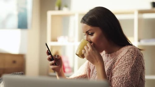 Woman Uses Phone and Drinks Coffee at Home